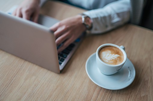 Close-up shot of a businesswoman with a laptop and a cup of coffee sitting in a cafe