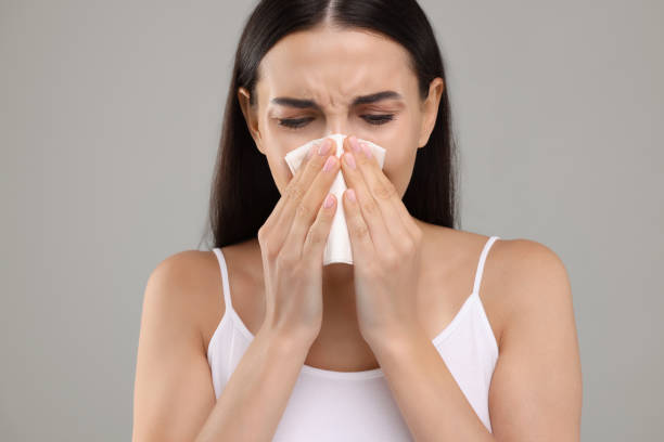 istock Suffering from allergy. Young woman blowing her nose in tissue on light grey background 1943304521