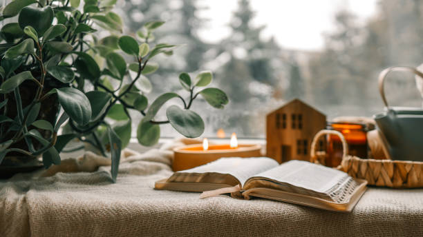 istock Cozy winter photo, stack of sweaters, open Bible, tea and candle 1943332579