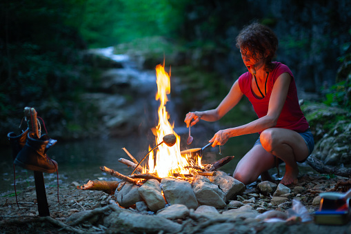 Female Determinate Hiker Roasting Potatoes on a Campfire in Wilderness