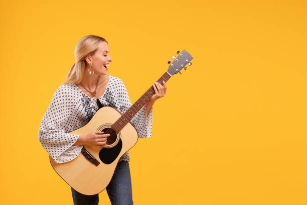 istock Happy hippie woman playing guitar on yellow background. Space for text 1943342517