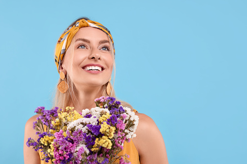 Portrait of smiling hippie woman with bouquet of flowers on light blue background. Space for text