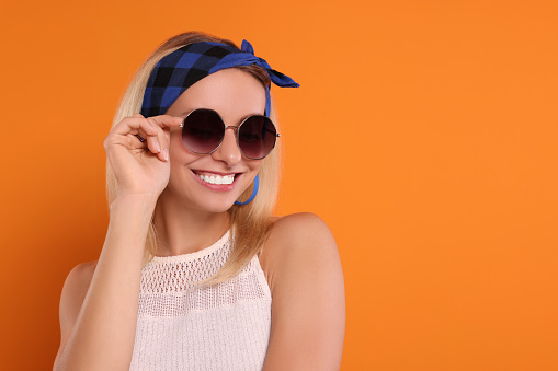 Portrait of smiling hippie woman in sunglasses on orange background. Space for text