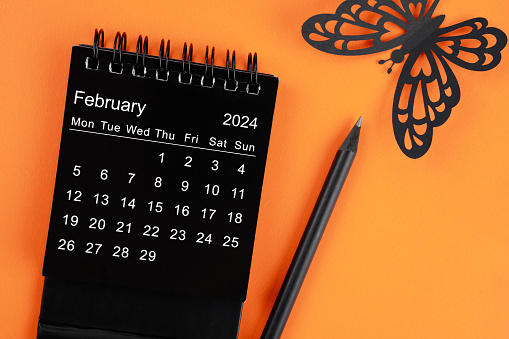February 2024 desk calendar for the organizer to plan and reminder and butterfly paper on orange color background.