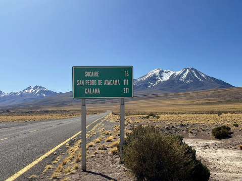 Signpost on Route 23 in the Atacama Desert with snow-capped volcanoes in the background.