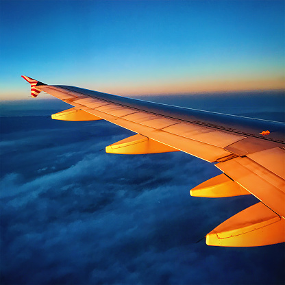 This photograph captures the wing of a large commercial airplane bathed in the warm glow of sunlight, set against a backdrop of a serene sky and clouds.