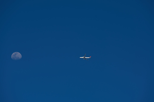 Photo of the moon and an airplane late afternoon with blue skies as background