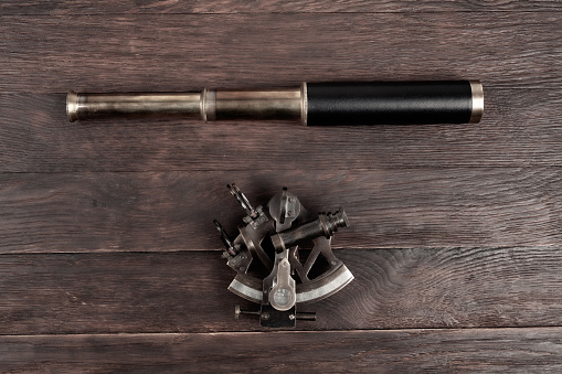 Retro vintage spyglass telescope with sextant on wooden background