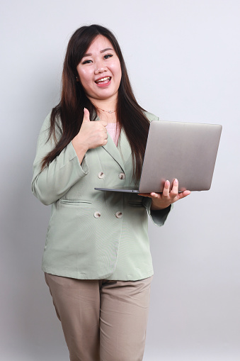 Portrait of Confident Female Worker Wearing Formal Wear Holding Laptop and Showing Thumbs Up for Recommendation Gesture