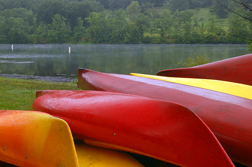 Red and yellow canoes are piled along the lake shore of a camp in the summer