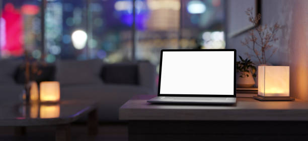 istock A white-screen laptop computer and a table lamp on a table in a modern, dark living room at night. 1943745170