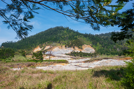 Kawah Sikidang (Sikidang Crater) in Dieng Plateau, Central Java, Indonesia. The with sulphur smoke floating is coming out from the crater. A tree as a foreground frame.