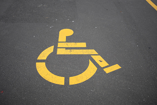 Disabled carparking logo painted yellow on asphalt pavement