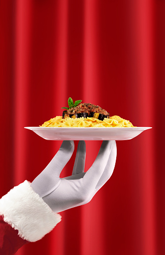 Santa serving pasta with sauce in front of a red curtain