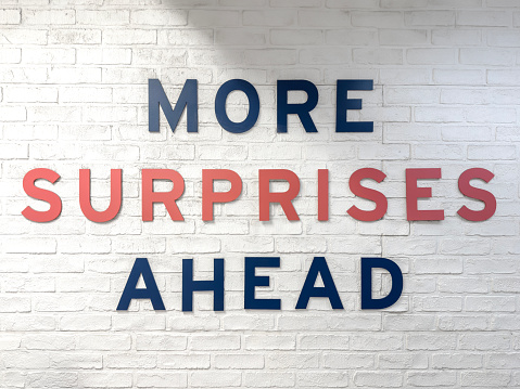 More surprises ahead sign on a white painted brick wall