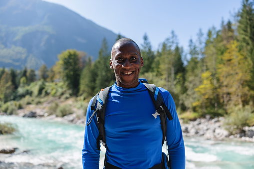 Smiling African hiker enjoying outdoor activity with mountain river and greenery in the background