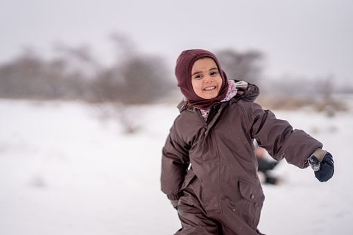A sweet little girl is seen running through the snow as she enjoys the cool fresh air.  She is dressed warmly in a snowsuit, boots, hat and mittens as she joyfully plays.