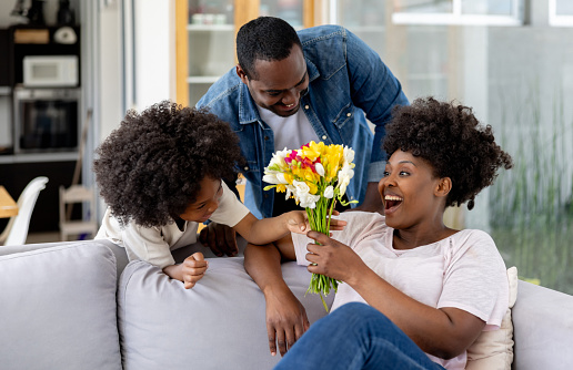 Happy African American family surprising mom with flowers on Mother's  Day - special event concepts