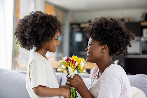 Loving African American girl surprising mom with flowers on Mother's Day - special event concepts