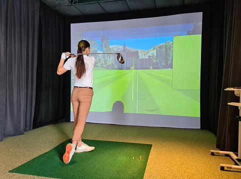 Female golfer plays golf on golf simulator. Indoor golf