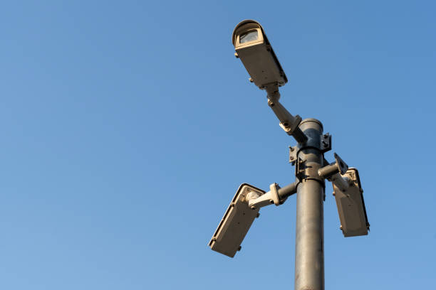 istock Group of three security cameras mounted on a tall, metal pole. The pole is also white, with a black base.The cameras are positioned at different angles. 1943891177