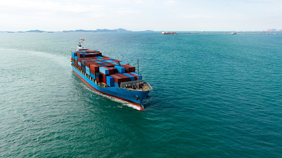 logistic cargo container ship sailing in sea to import export goods and distributing products to dealer and consumers across worldwide, aerial front view from drone,