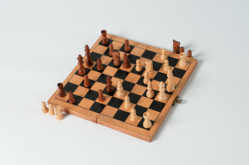 The chess game board in the photo has a light base where the white and black chess pieces face each other