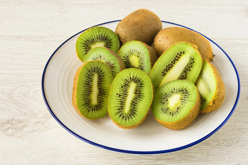 On a white plate lies a fresh juicy kiwi cut in half.