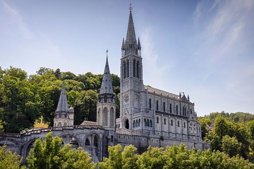 Famous Sanctuary of Our lady of Lourdes - Rosary Basilica Panorama under blue summer sky. World famous Pilgrim destination. Cathedral of Lourdes next to river Gave de Pau. Lourdes is a small town lying in the foothills of the Pyrenees, famous for the Maria apparitions of Our Lady of Lourdes. Our Lady of Lourdes Basilica in Lourdes, Lourdes,  Hautes-Pyrenees, France, Europe