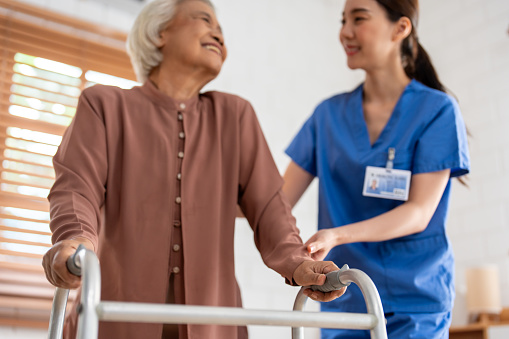 Asian senior older woman patient doing physical therapy with caregiver. Attractive specialist carer women help and support elder mature female practice walking slowly with walker at nursing home care.