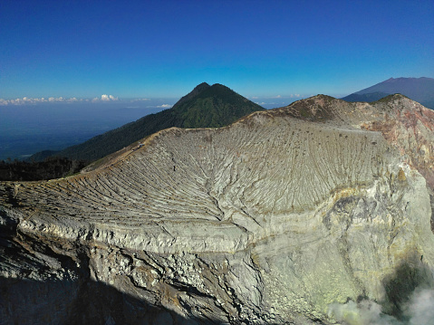 Stunning Ijen volcano mountain landscape with a crater rock mountain, lush vegetation, a valley, and a clear blue sky.