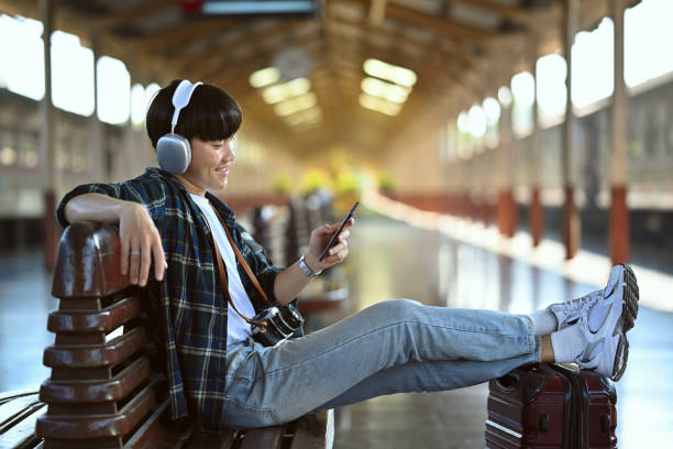 istock Happy young man in headphone using mobile phone during waiting for train at railway station 1944175950