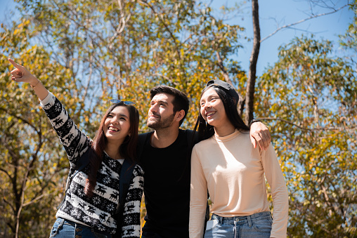 Happy Multi-ethnicity group of young enjoy hiking ,walking, exploring in forest on vacation, Caucasian man and Asian female having fun in forest beautiful autumn day. spend time together in holidays.