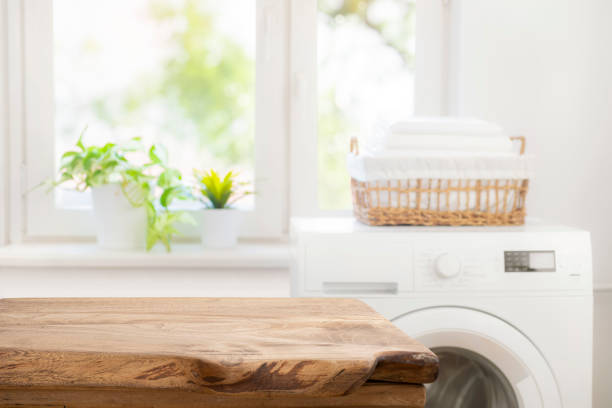 istock Aged wooden table for product display on blur washing machine in laundry room background 1944227304