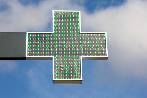 green cross on shop pharmacy facade of a building in cloud blue sky in medical symbol