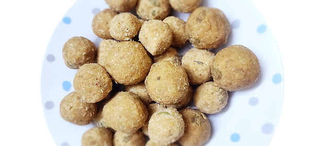 Cut out of Horizontal picture of a heap of homemade aata laddoos or aatta laddu mithai plated in a spotted white plate or dish bowl isolated over white background