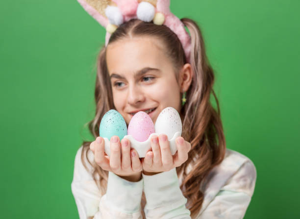 happy easter. funny cute girl with easter bunny ears and colorful easter eggs on green background. copy space. - easter easter bunny fun humor stock-fotos und bilder