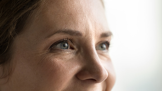 Blue eyes of young middle aged woman with black mascara on eyelashes looking away, smiling, laughing. Cropped shot banner. Female model upper face with natural makeup, dry facial skin with wrinkles