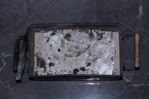 Cold or extinguished ashes in a iron barbeque on a marble floor, wide
