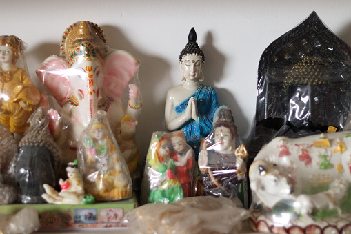 Bunch of religious ceramic statue of Hindu and Buddhism in a shelf on white wall