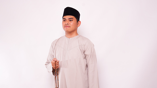 Asian muslim man holding prayer beads and praying against white background
