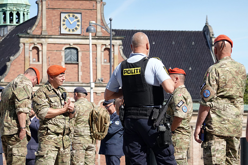 Danish police officer and 5 military men working together and controlling the area around Christiansborg Palace, - the dansih government, building on a sunny day in Copenhagen, Denmark