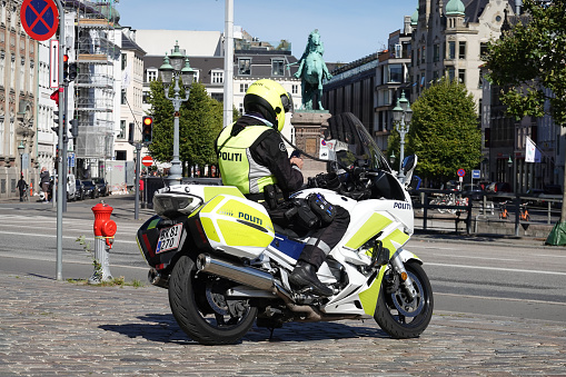 Danish policeofficer fully equipped looking on his phone on a policemotorbike in front of the danish Government Building of Christiansborg on a sunny day in Copenhagen, Denmark