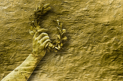 Hand holds a laurel wreath - concept image against a golden colored background - Success and fame concept image with copy space.