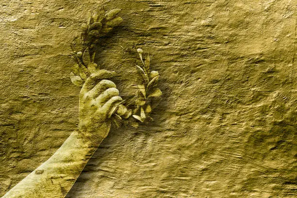 Photo of Hand holds a laurel wreath - concept image against a golden colored background - Success and fame concept image with copy space