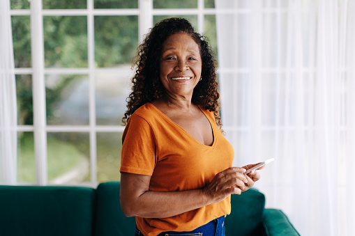 Portrait of a happy and connected senior woman at home, who uses her smartphone to stay in touch with her loved ones, navigate the digital world, and enjoy her leisure time.