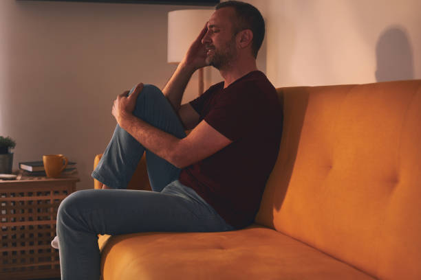 istock Man with headache and knee pain sitting on a sofa at home. 1944338616