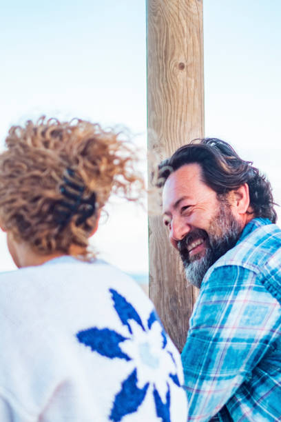 vista lateral de una pareja madura feliz que disfruta del tiempo juntos en actividades de ocio al aire libre con la playa en el fondo. actividad turística de personas. hombre sonriendo a la mujer. colores azules, estado de ánimo y copiar espacio, cielo - honeymoon beach couple heterosexual couple fotografías e imágenes de stock