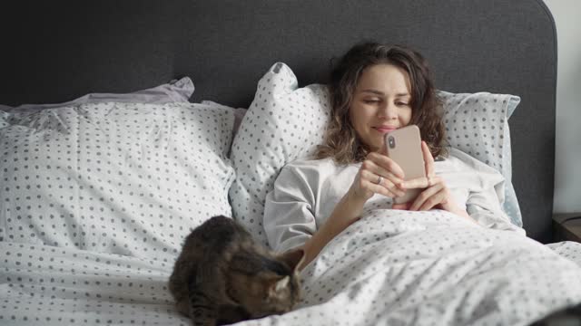 A young Caucasian woman uses her phone lying in bed