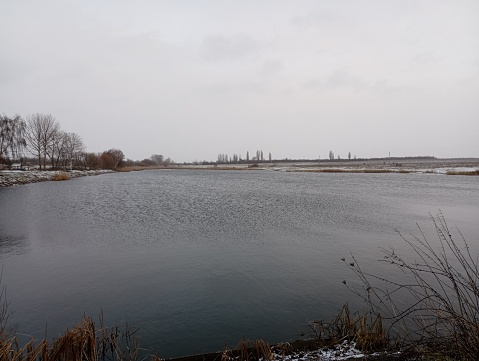 A beautiful view of a large lake in cloudy winter weather. A beautiful reservoir with a calm water surface. Fishing and recreation by the water.